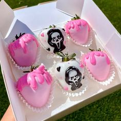 six decorated strawberries are in a box on the grass, with pink and black frosting