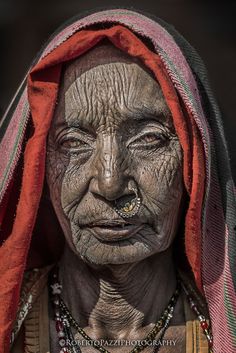 an old woman with wrinkles on her face and red scarf over her head, looking at the camera