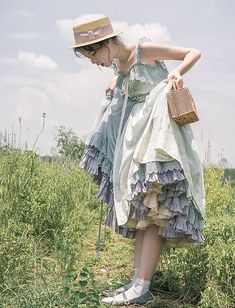 a woman in a dress and hat is standing on the side of a hill holding a basket