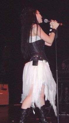 a woman with long black hair and white dress on stage holding a microphone in her hand