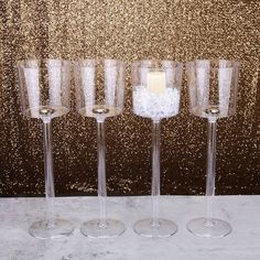 four wine glasses with candles in them sitting on a white tablecloth next to a gold glitter wall