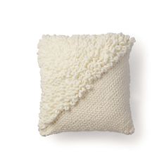 a white knitted pillow on a white background with a blanket folded over the top