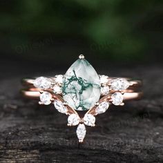 a green and white stone ring sitting on top of a piece of wood with diamonds