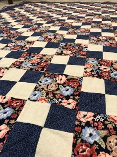 a blue and white checkered quilt with flowers on the bottom, in front of a wooden bench