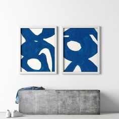 two blue and white paintings hanging on the wall next to a bed in a room