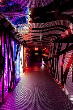 a long hallway with colorful lights and patterns on the ceiling, leading to another room