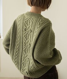 a young boy wearing a green sweater standing in front of a window with his back turned to the camera