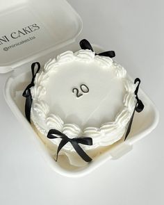 a white cake with black ribbon and the number 20 on it in a plastic container