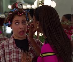 a woman is getting her hair done in the mirror while another woman brushes her hair