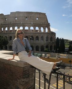 a woman sitting on top of a brick wall next to an old building with a roman collise in the background