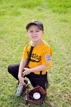 a young boy sitting in the grass with a baseball glove