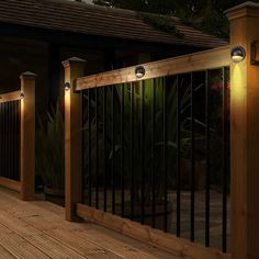 two lights are on the side of a wooden deck near a fence and planter