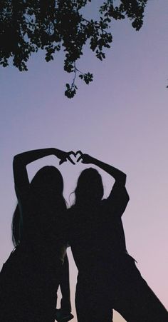 two women standing next to each other with their arms in the shape of a heart