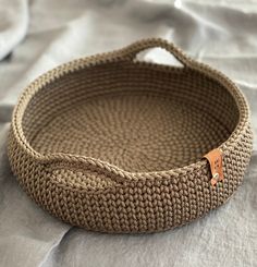 a woven basket with a leather tag on the handle sitting on a white bed sheet