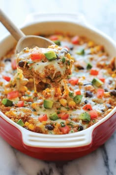 a spoon full of mexican chicken casserole on a marble counter with a red dish