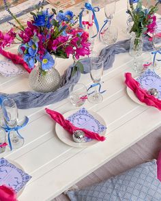 the table is set with purple and blue flowers in vases, napkins, and wine glasses