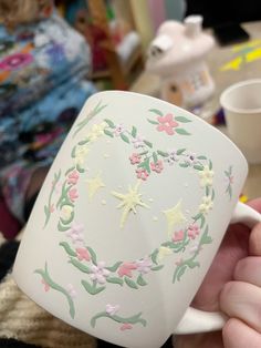 a hand holding a white coffee mug decorated with pink and green flowers