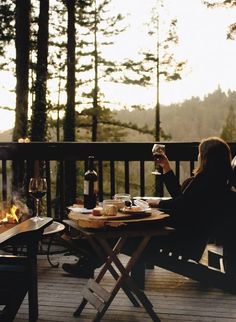 a woman sitting at a table on top of a wooden deck next to a fire pit