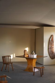 an empty room with two wooden chairs and a table in front of a wall sculpture