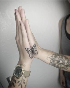 two hands with tattoos on them are holding a watch and butterfly tattoo is on the wrist