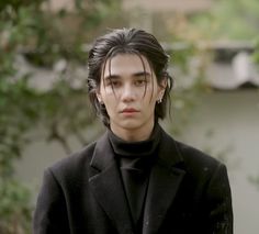 a young man with black hair wearing a coat and turtle neck sweater looking at the camera