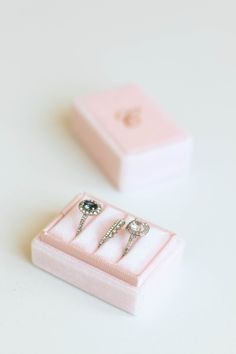 two wedding rings in a pink box on top of a white table next to each other