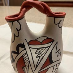 a ceramic vase sitting on top of a white cloth covered table next to a window