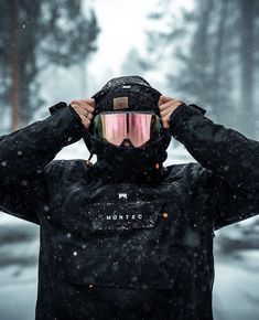 a man wearing ski goggles and a jacket in the snow with his hands on his head