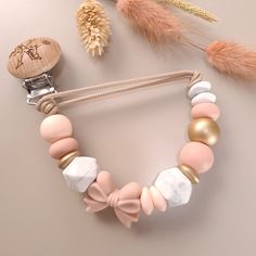 a necklace with pink, white and gold beads on a string next to feathers in the background