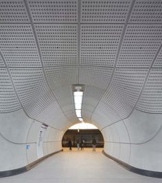 people are walking through a tunnel with white perfored walls and flooring on either side