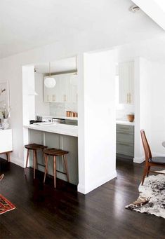 an open kitchen and living room with white walls, wood flooring and wooden chairs