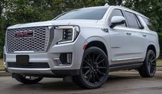 the front end of a white gmc suv parked in a driveway next to trees