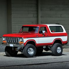 a red and white pickup truck parked on the side of a road next to a building