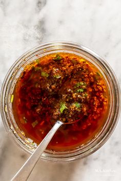 a glass bowl filled with soup on top of a white counter next to a spoon