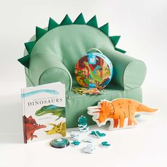 a dinosaur toy sitting on top of a green chair next to a book and toys