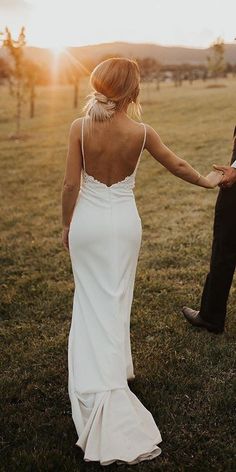 a bride and groom hold hands as the sun sets behind them in an open field