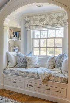 a window seat with pillows on it in front of a book shelf and bookshelf