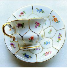 a fancy tea cup and saucer with gold trimmings on the rim, decorated with colorful flowers