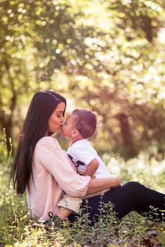 a woman holding a small child in her lap while sitting on top of a grass covered field