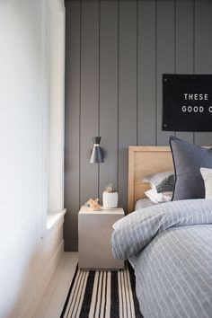 a bedroom with gray walls and striped bedding is pictured in this image, there is a good sign above the bed