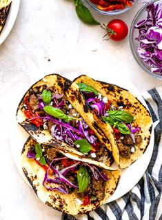 three tacos on a plate with red cabbage and tomatoes