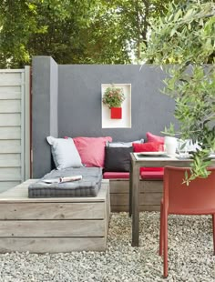 an outdoor seating area with red and grey cushions on the bench, table and chairs