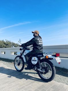 a man riding on the back of a motorcycle down a street next to a white fence