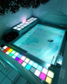 an overhead view of a swimming pool with colored tiles and lights on the bottom floor