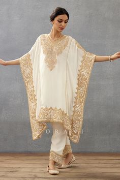 Ivory kaftan with placement vintage pattern, cut work lace hem details, contrast gold dori, sequin, adda hand embroidered yoke and borders. Paired with pants with embroidered border.
Components: 2
Pattern: Hand Embroidered
Type Of Work: Dori, Sequin, Lace and Adda Work
Neckline: V Neck
Sleeve Type: Flared Sleeves
Fabric: Silk Crepe, Cotton Voile
Color: Ivory
Other Details: 
Cut work lace hem
Printed inner border
Occasion: Destination Wedding,Sangeet - Aza Fashions Embroidery Kaftan, Designer Kaftan, Kaftan Set, Dori Embroidery, Lace Kaftan, Embroidered Kaftan, Dangler Earrings, Party Wear Indian Dresses, Ivory Silk