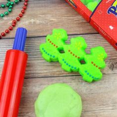 green play dough next to an orange plastic marker and red beaded necklace on a wooden table