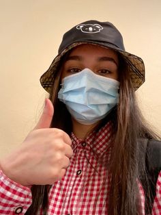 a woman wearing a face mask gives the thumbs up sign with her thumb and hat on