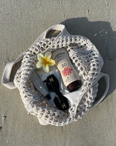 the contents of a beach bag are laid out on the sand, including sunscreen and sunglasses