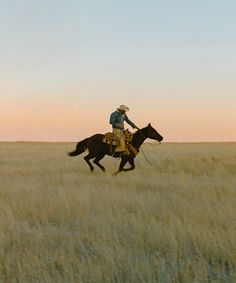 a man riding on the back of a black horse in a field at sunset or dawn