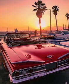 an old red car parked in front of palm trees on the beach at sunset or sunrise